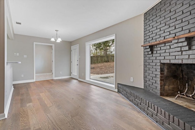 unfurnished living room featuring hardwood / wood-style flooring, a brick fireplace, and a chandelier