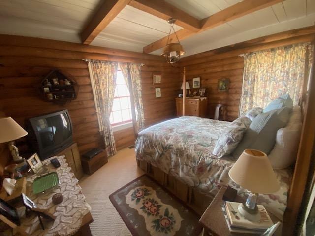 bedroom with beamed ceiling, rustic walls, a chandelier, and light carpet