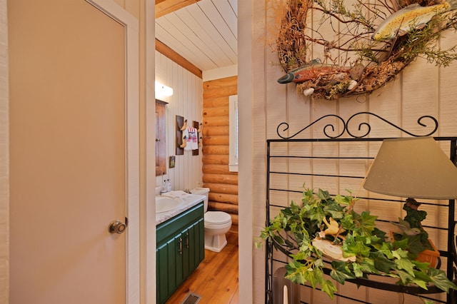 bathroom featuring wood-type flooring, toilet, rustic walls, and vanity