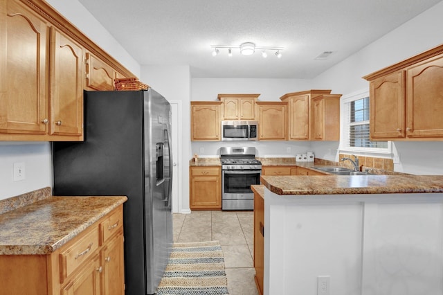 kitchen with sink, light tile patterned floors, appliances with stainless steel finishes, a textured ceiling, and kitchen peninsula