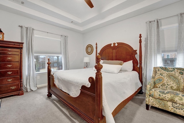 carpeted bedroom with a raised ceiling and ceiling fan