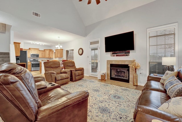 living room featuring a tiled fireplace, ceiling fan with notable chandelier, and high vaulted ceiling