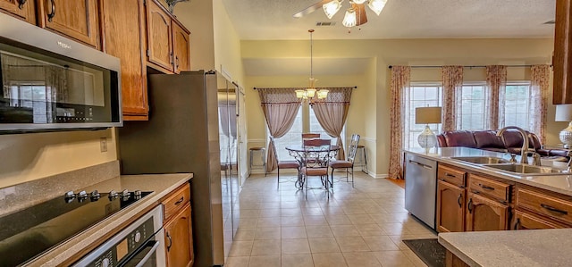 kitchen with sink, a textured ceiling, light tile patterned floors, appliances with stainless steel finishes, and pendant lighting