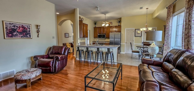 living room featuring sink, ceiling fan with notable chandelier, vaulted ceiling, and light wood-type flooring