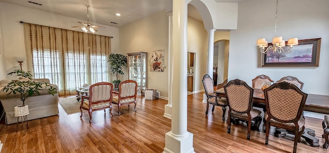 dining space featuring ornate columns, wood-type flooring, a high ceiling, and ceiling fan with notable chandelier