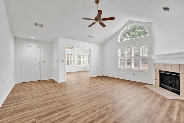 unfurnished living room featuring ceiling fan, high vaulted ceiling, a tile fireplace, and light wood-type flooring