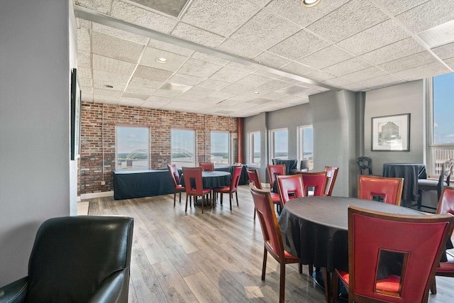 dining area featuring wood-type flooring, a paneled ceiling, plenty of natural light, and brick wall