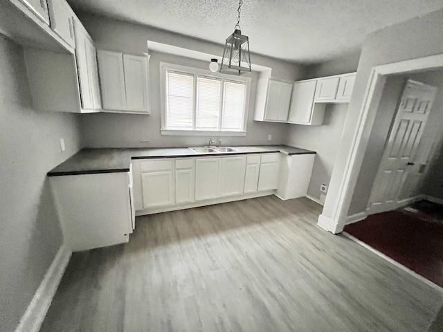 kitchen featuring sink, light hardwood / wood-style flooring, a textured ceiling, pendant lighting, and white cabinets