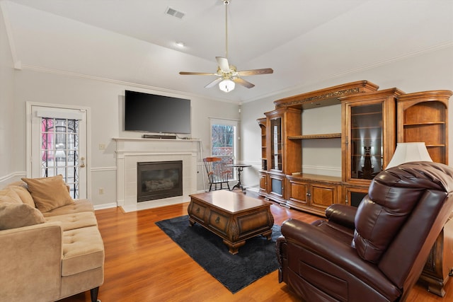 living room featuring ceiling fan, ornamental molding, a tiled fireplace, and light hardwood / wood-style floors