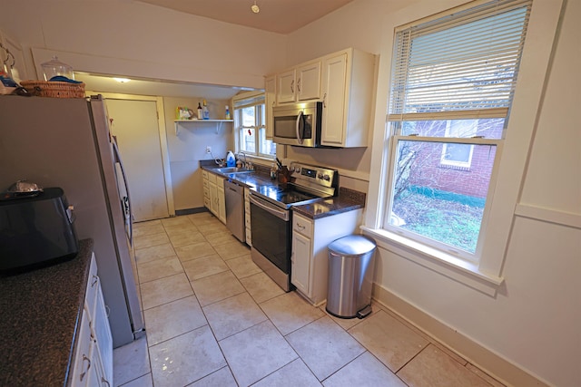 kitchen with sink, white cabinetry, dark stone countertops, light tile patterned floors, and appliances with stainless steel finishes