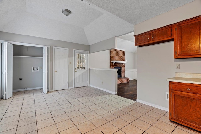 kitchen with lofted ceiling, a brick fireplace, a textured ceiling, and light tile patterned flooring