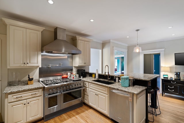 kitchen with appliances with stainless steel finishes, sink, a kitchen breakfast bar, hanging light fixtures, and wall chimney exhaust hood