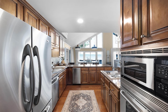 kitchen featuring appliances with stainless steel finishes, lofted ceiling, sink, backsplash, and kitchen peninsula