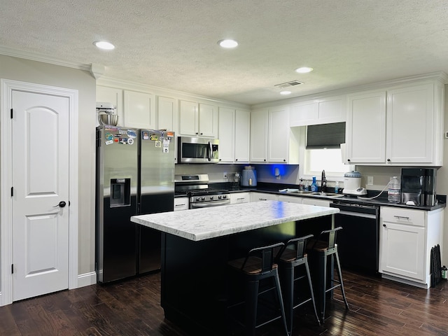 kitchen featuring sink, dark wood-type flooring, appliances with stainless steel finishes, white cabinets, and a kitchen island