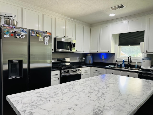 kitchen with sink, white cabinetry, stainless steel appliances, a center island, and a textured ceiling