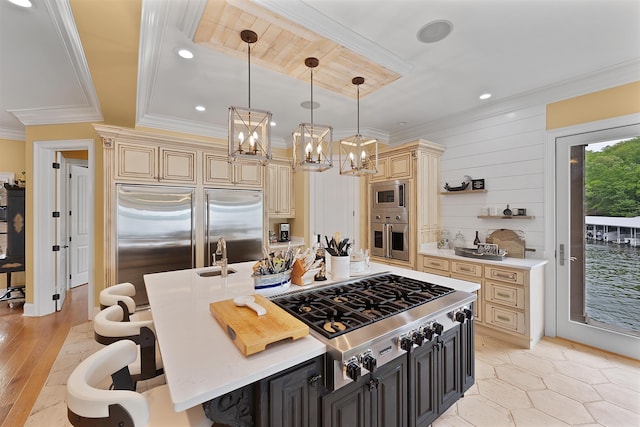 kitchen with pendant lighting, a kitchen bar, built in appliances, ornamental molding, and a center island with sink