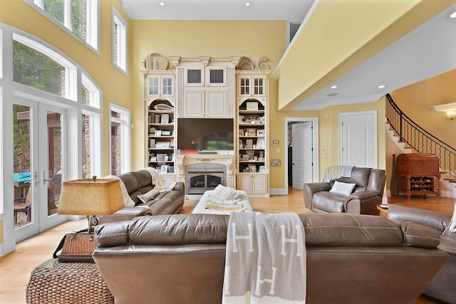 living room featuring a towering ceiling, a premium fireplace, ornamental molding, and light hardwood / wood-style flooring