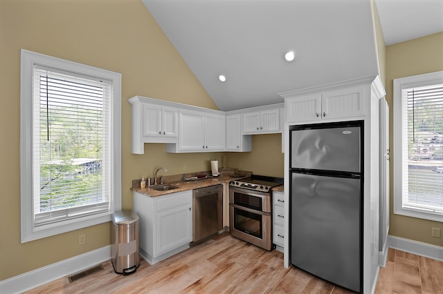 kitchen with lofted ceiling, sink, stone countertops, stainless steel appliances, and white cabinets