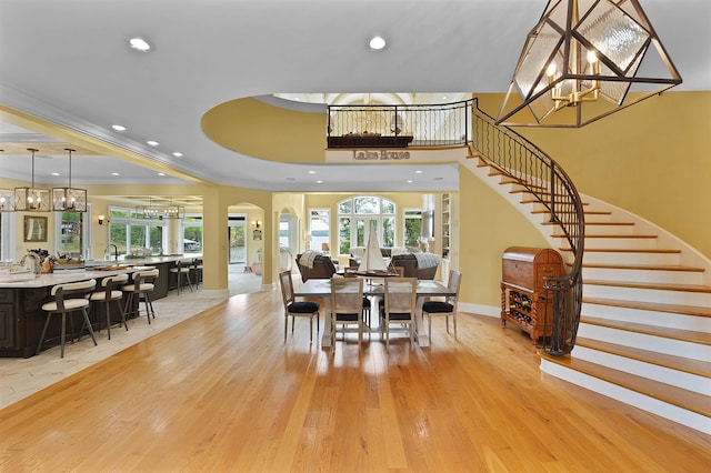 dining room featuring an inviting chandelier, ornamental molding, a raised ceiling, and light wood-type flooring