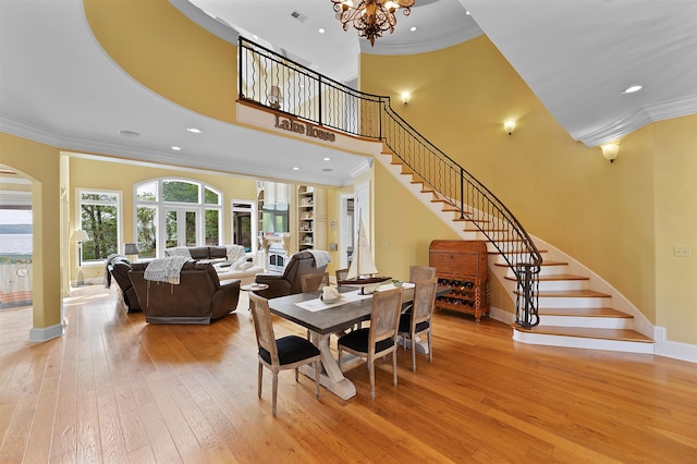 dining area featuring a high ceiling, crown molding, an inviting chandelier, and light hardwood / wood-style flooring