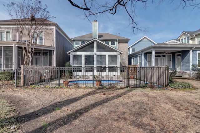 rear view of property with ceiling fan, a fenced in pool, and a sunroom