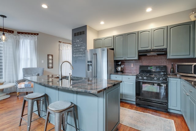 kitchen featuring sink, hanging light fixtures, stainless steel appliances, and an island with sink