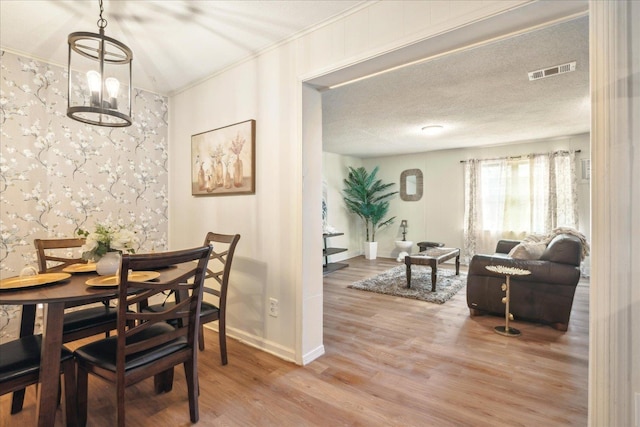 dining area featuring wood-type flooring, crown molding, an inviting chandelier, and a textured ceiling