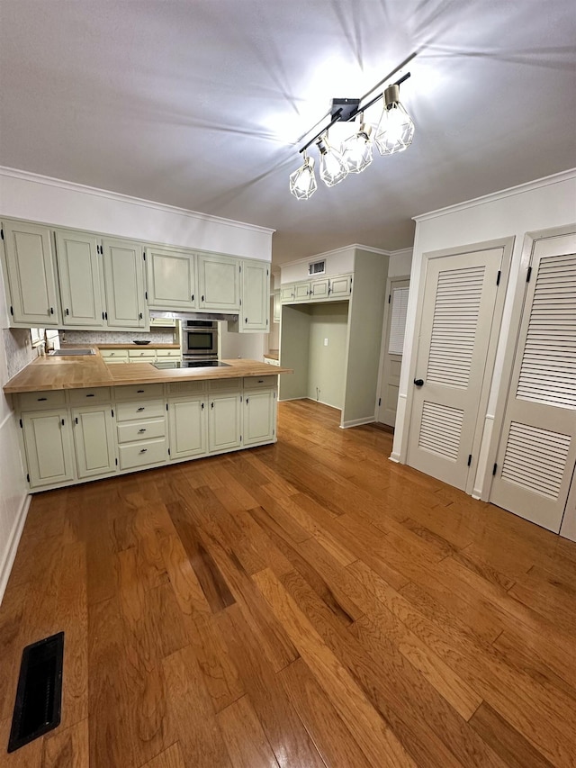 kitchen featuring backsplash, black stovetop, ornamental molding, light hardwood / wood-style floors, and kitchen peninsula