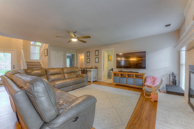 living room featuring ceiling fan, light hardwood / wood-style flooring, and a textured ceiling