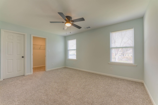 unfurnished bedroom with a walk in closet, light carpet, ceiling fan, and a closet