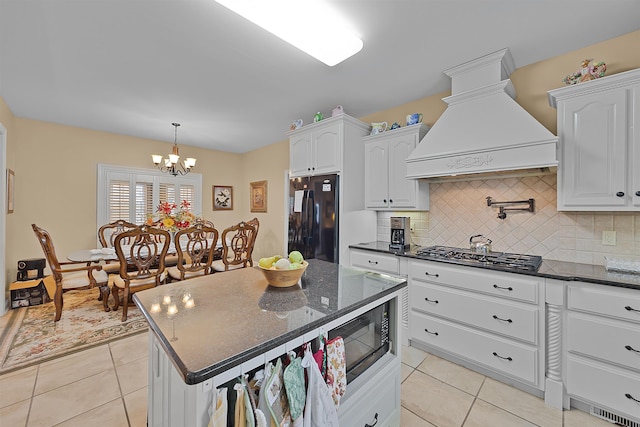 kitchen featuring tasteful backsplash, black appliances, white cabinets, and premium range hood