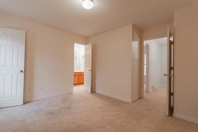 unfurnished bedroom featuring light carpet, a textured ceiling, and ensuite bath