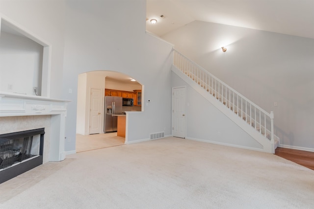 unfurnished living room with a tile fireplace, light colored carpet, and high vaulted ceiling