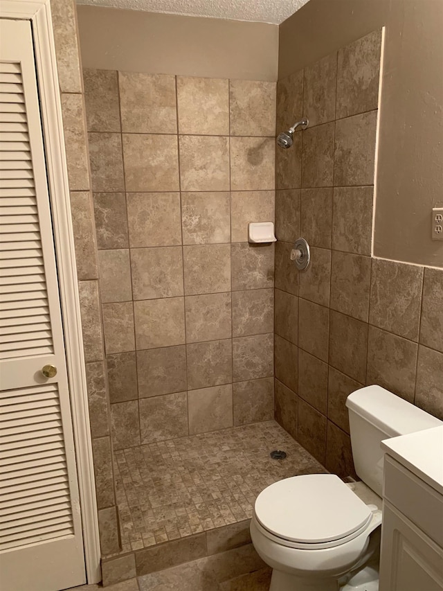 bathroom featuring toilet, tile walls, a textured ceiling, a tile shower, and vanity