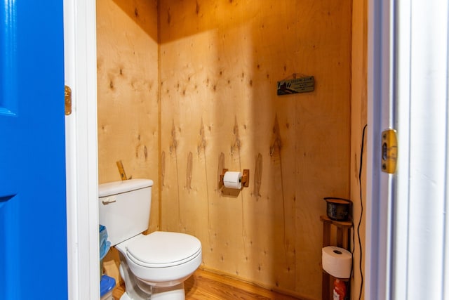 bathroom with hardwood / wood-style floors, wood walls, and toilet