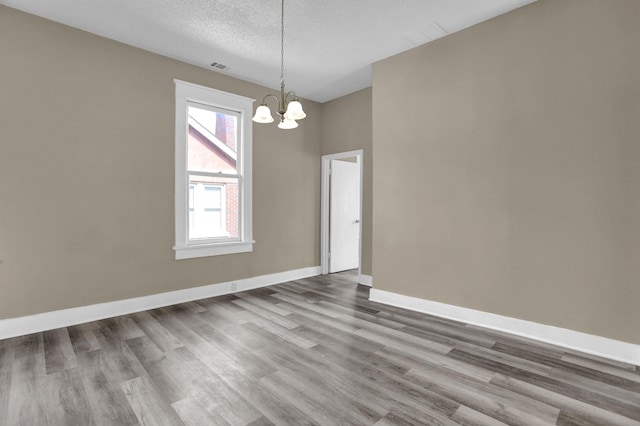 spare room with an inviting chandelier, hardwood / wood-style floors, and a textured ceiling