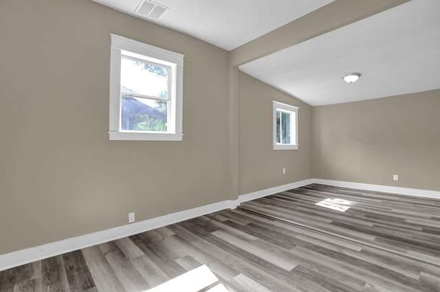 empty room featuring vaulted ceiling, plenty of natural light, and hardwood / wood-style floors