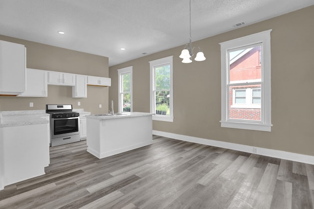 kitchen featuring sink, white cabinetry, hanging light fixtures, stainless steel range with gas stovetop, and an island with sink