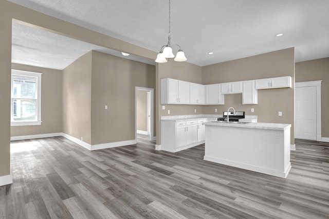 kitchen featuring an island with sink, pendant lighting, light stone countertops, hardwood / wood-style floors, and white cabinets