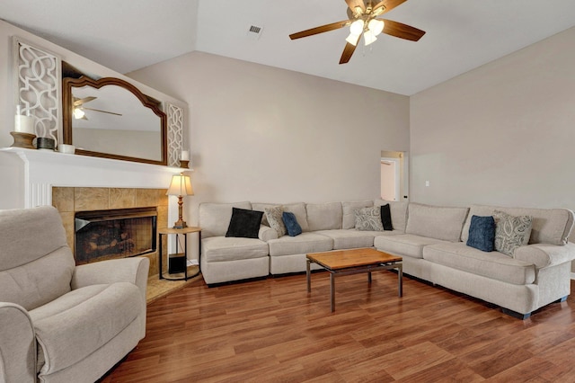 living room with a tiled fireplace, wood-type flooring, lofted ceiling, and ceiling fan