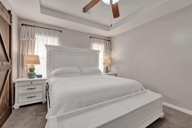 bedroom with a raised ceiling, multiple windows, and dark colored carpet