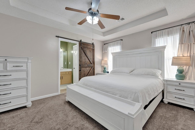 bedroom featuring a barn door, carpet flooring, a textured ceiling, and a tray ceiling