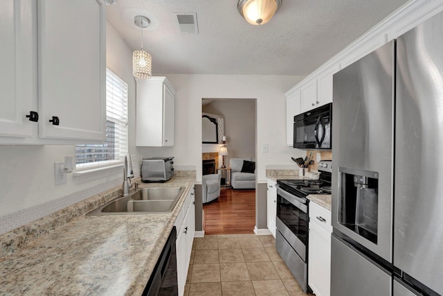 kitchen with white cabinetry, sink, decorative light fixtures, and black appliances