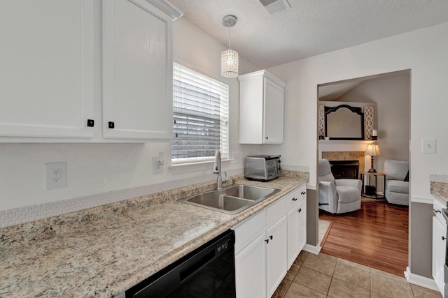 kitchen featuring sink, a tile fireplace, white cabinetry, hanging light fixtures, and black dishwasher