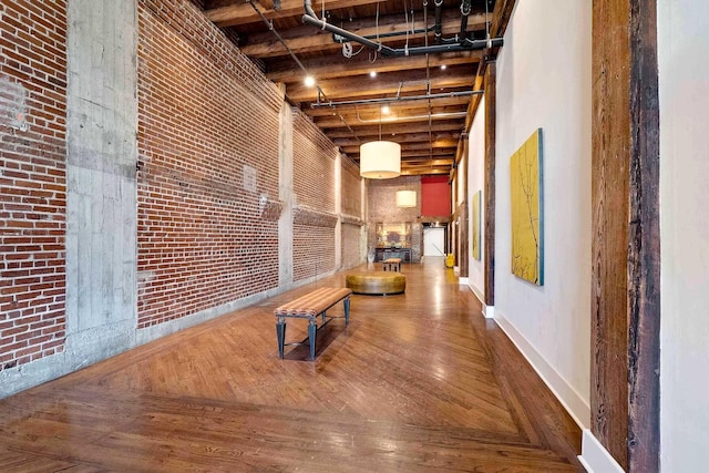 hall with hardwood / wood-style flooring, brick wall, and a high ceiling