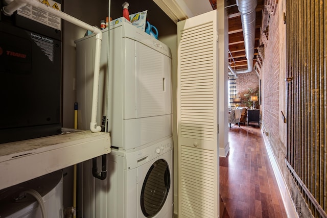 laundry area with brick wall, stacked washer / drying machine, and hardwood / wood-style floors