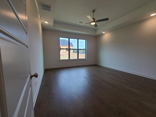 empty room featuring a raised ceiling, ceiling fan, and dark hardwood / wood-style flooring