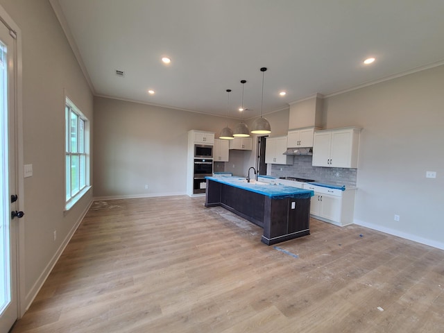 kitchen featuring gas stovetop, white cabinetry, decorative light fixtures, a center island with sink, and stainless steel microwave