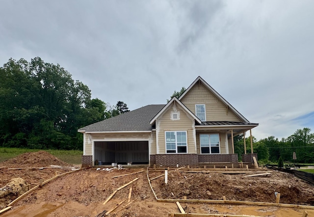 craftsman-style home with covered porch, a standing seam roof, driveway, brick siding, and an attached garage