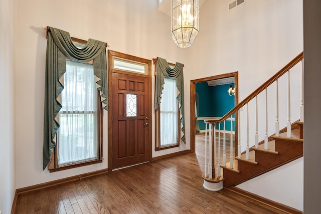 foyer featuring an inviting chandelier, a towering ceiling, visible vents, stairs, and wood-type flooring